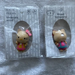 Hello Kitty Trä Kylskåpsmagnet  - Fyra små kylskåpsmagneter i trä, formade som katter med rosa rosett och olika färgglada kläder. Figurerna har målade detaljer som svarta morrhår och gula nosar. Perfekt för att dekorera kylskåpet med en gullig touch. 55kr/2st / bild 