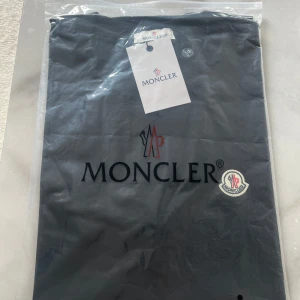 Svart Moncler t-shirt med logga - Snygg svart t-shirt från Moncler med klassisk logga på bröstet och rund hals. T-shirten är enkel men stilren, perfekt för dig som gillar exklusiva märken och vill ha en clean look. Tillverkad i mjuk bomull för skön känsla hela dagen.