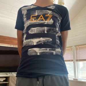 Mörkblå EA7 t-shirt från Armani  - Snygg mörkblå t-shirt från Armani  med EA7-tryck i gult och grått mönster framtill. Klassisk passform med korta ärmar och rund hals. Perfekt för dig som gillar streetstyle och vill sticka ut med ett coolt print. Den används inte längre då den kom som present