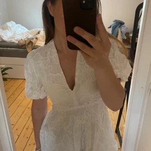 Vit kort klänning från Zara - Superfin vit kort klänning från Zara med broderade blommor, puffiga korta ärmar och djup v-ringning. Storlek s men passar mycket mer xs skulle jag säga 