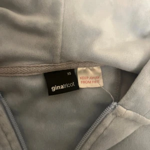 Ljusblå velour hoodie från Gina Tricot - Mjuk och skön ljusblå hoodie i velour från Gina Tricot. Tröjan har dragkedja framtill, huva med snörning och känguruficka. Perfekt för en chill och avslappnad stil. Långärmad och i en loose passform.