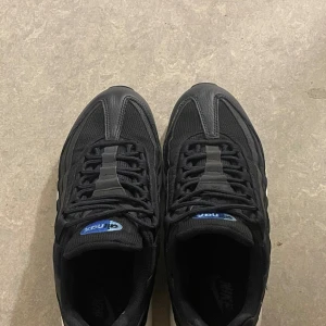 Nike Air Max 95 svart/blå sneakers - Letar du efter ett par stilrena och bekväma sneakers? Här har du ett par Nike Air Max 95 i svart med blå detaljer – en klassiker som aldrig går ur tiden! Produktbeskrivning 	•	Modell: Nike Air Max 95 	•	Färg: Svart med blå detaljer och vit sula 	•	Storlek: (ange din storlek här) 	•	Skick: Mycket bra, endast lätt använda. Inga större skador eller fläckar. 	•	Komfort: Den ikoniska Air Max-dämpningen ger skön komfort hela dagen. 	•	Stil: Passar både till vardags och till träning