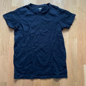 Svart basic t-shirt från 157 - En svart, klassisk t-shirt från 157 i 100% bomull. Enkel och stilren design med rund hals och korta ärmar. Perfekt för dig som gillar en clean och tidlös look. Passar till allt och är superbekväm att bära.