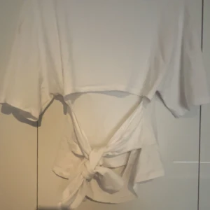 Vit omlottopp med knyt i midjan - Jag säljer den för att den var för stor på mig, endast provad.  Säljer en vit omlottopp med korta ärmar och snygg knytning i midjan. Toppen har en avslappnad passform och är perfekt för dig som gillar stilrena och enkla plagg med en twist. Gjord i mjukt bomullstyg som känns skönt mot huden.