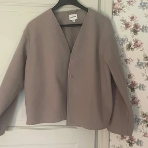 Beige kappa från Kappahl, V-ringad - Stilren beige kappa från Kappahl i storlek M. Jackan har en minimalistisk design med V-ringning, enkel knäppning framtill och långa ärmar. Perfekt för dig som gillar en clean look och vill ha något som funkar till många outfits.