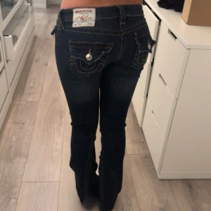 True Religion mörkblå bootcut jeans - Snygga mörkblå jeans från True Religion med bootcut passform och ikoniska fickdetaljer bak. Låg midja, klippta för att passa mig i längden. De passar bra på mig som är 158. Strl är 24. Knappt använda!!