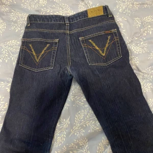 Mörkblå bootcut fleard jeans från Vila - Snygga mörkblå jeans från Vila med bootcut passform. Jeansen har klassiska gula kontrastsömmar och coola V-detaljer på bakfickorna. Tillverkade i jeansmaterial och perfekta för dig som gillar en tidlös look med lite extra edge.