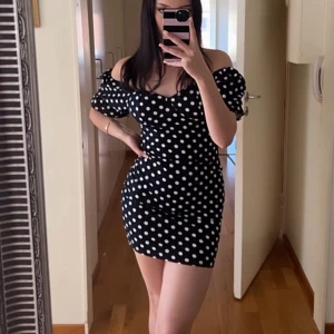 Svart prickig kortklänning med puffärm - Supersöt svart kortklänning med vita prickar och puffiga kortärmar. Klänningen har en figurnära passform och söt sweetheart-urringning. Perfekt för dig som gillar retrovibbar och vill sticka ut lite extra.