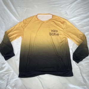 Gul-svart långärmad tröja Vero Brava - Snygg långärmad tröja från Vero Brava med gul till svart ombre-effekt. Tröjan har rund halsringning och tryckt logga på bröstet. Perfekt för dig som gillar streetstyle och vill sticka ut med cool färgövergång.