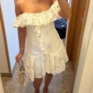 Vit offshoulder spetsklänning - Superfin vit kortklänning med offshoulder och volangdetaljer( man kan ha den över axlarna också). Klänningen har spetsmönster och en romantisk vibe, perfekt för sommarkvällar. Den är figurnära upptill och har en utsvängd kjol med extra volym. Använt en gång är 158cm