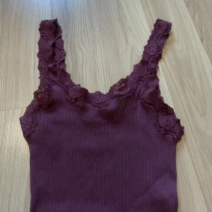 Vinröd spetsklänning från Rosemunde - Supersöt vinröd kortklänning från Rosemunde med ribbad struktur och breda spetsband. Klänningen är ärmlös och har vacker spetsdetalj längs urringningen och axelbanden. Materialet är en mix av silke och bomull för en mjuk och lyxig känsla.