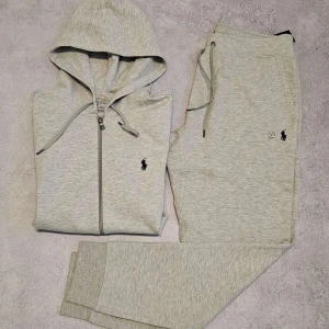 Ljusgrå hoodie från Polo Ralph Lauren - Snygg ljusgrå hoodie från Polo Ralph Lauren med dragkedja och huva. Klassisk logga broderad på bröstet. Mjuk bomullsblandning och ribbade muddar. Perfekt för chill dagar eller när du vill vara bekväm men ändå stilren.