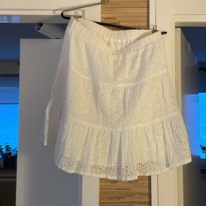 Vit volangkjol från SHEIN - Superfin vit kortkjol från SHEIN med broderade hål och volangkant. Kjolen har resår i midjan och är fodrad för extra komfort. Perfekt för sommarens alla tillfällen och ger en söt och luftig vibe.