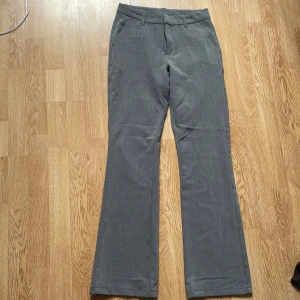 Grå kostymbyxor från Lindex, stl 170 - Snygga grå kostymbyxor från Lindex i storlek 170. Byxorna har raka ben med lätt utsvängd bootcut. Helt oanvända med prislappen på.