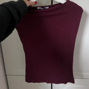 Vinröd ärmlös topp från H&M - En enkel och stilren vinröd topp från H&M. Modellen är ärmlös med rund halsringning och har en tight passform. Perfekt att matcha med jeans eller kjol för en clean look. Materialet är mjukt och stretchigt, vilket gör den superbekväm.