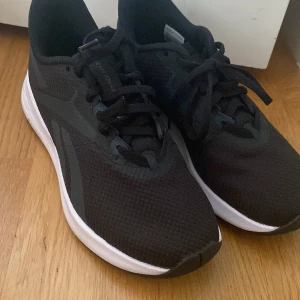 Svarta Reebok sneakers med vit sula - Snygga svarta Reebok sneakers med vit sula och diskret logga på hälen. Ovandelen är i mesh för extra andningsförmåga och komfort, med klassisk snörning och rund tå. Perfekta för träning eller en sportig look till vardags. Dem är som nya
