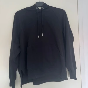 Svart hoodie från H&M Basics - En svart hoodie från H&M Basics i storlek M. Klassisk modell med huva och snörning, samt en stor känguruficka framtill. Tröjan har långa ärmar och ribbade muddar. Perfekt för chill dagar eller när du vill ha en enkel och stilren look. Kontakta för fler bilder eller frågor!