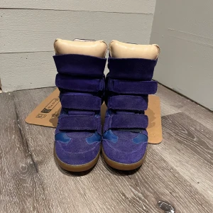 Isabel Marant Skor - Isabel Marant i mörkblå mocka och textil med högt skaft och inbyggd kilklack. Skorna har flera breda kardborreband framtill och en brun gummisula. Skorna är nästintill heltnya. Om man kollar inuti skorna ser man att det är lite tecken på användning.