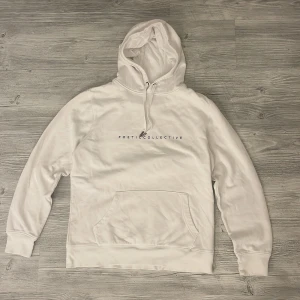 Vit hoodie Poetic Collective  - Vit hoodie från Poetic Collective i bomull med tryckt logga framtill och stor färgstark grafisk print på ryggen i blått, rött och svart. Klassisk känguruficka, dragsko i huvan och ribbade muddar. Perfekt för dig som gillar streetwear vibes.