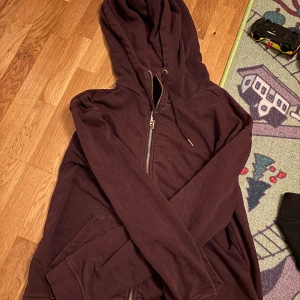 Mörklila hoodie med dragkedja från SOC - Säljer en mörklila hoodie från SOC i storlek S. Tröjan har huva med snörning, hel dragkedja framtill och två fickor. Perfekt för chill dagar eller när du vill ha något bekvämt och snyggt. Materialet är mjukt och känns skönt mot huden.