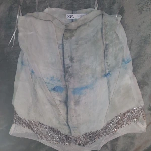 Paljettkantad linnetopp från Zara XS - Unik linnetopp från Zara i storlek XS med tunna axelband. Toppen har ett abstrakt mönster i beige, grått och blått samt en snygg kant med silvriga paljetter längst ner. Luftigt material som känns lyxigt och coolt, perfekt för att sticka ut. Använt flitigt. Den är i bra skick.