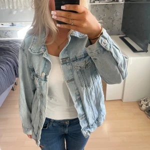 Ljusblå jeansjacka - Säljer en snygg ljusblå jeansjacka med knappar framtill och klassisk krage. Jackan har två bröstfickor med lock och knappar samt långa ärmar. Perfekt för en avslappnad stil.