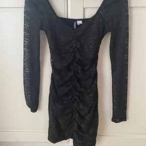 Svart klänning från H&M - Supersnygg svart kort spetsklänning från H&M med långärmad. Klänningen har blommigt spetsmönster, figurnära passform och rynkade detaljer framtill🩷Ändast testad och säljs då den aldrig kom till användning🩷 Nyskick🩷