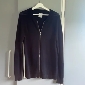 Svart kofta med dragkedja Clubs and Spades - En stilren svart kofta från Clubs and Spades i storlek medium. Koftan har lång ärm, ribbade muddar och hel dragkedja framtill. Perfekt för lager-på-lager och funkar året runt. Enkel och clean design som passar till det mesta.