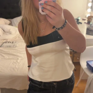 Vit och svart linnetopp - Snygg linnetopp i vitt med svart kant upptill. Toppen har en enkel och stilren design med raka linjer och smala axelband. Perfekt att matcha med jeans eller kjol för en clean look.