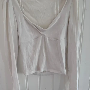 Vit långärmad v-ringad topp - Säljer en stilren vit/kräm vit långärmad topp med djup v-ringning och smickrande söm under bysten. Tunn och mjuk i materialet, rätt kort vid magen.