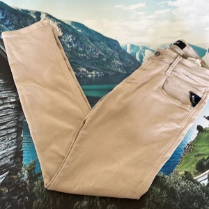 Beige Replay jeans med raka ben - Snygga beige jeans från Replay med klassisk femficksmodell och raka ben. Byxorna har bälteshällor, dragkedja och knapp framtill. Materialet är mjukt och skönt, perfekt för en avslappnad stil. Passar dig som gillar stilrena och neutrala färger.