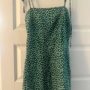 Grön blommig kortklänning med smala band - Supersöt grön kortklänning med vita småblommor och smala axelband som knyts. 💓💓