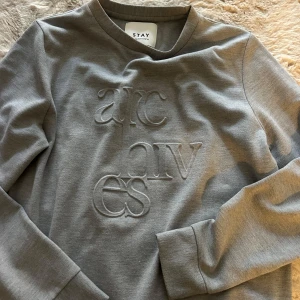 Grå sweatshirt - Snygg grå sweatshirt från STAY med upphöjd brodyrtext på framsidan. Tröjan har rund halsringning och långa ärmar. Passar mig som är S/M, om man vill ha lite overzised, så skulle mer säga det är en M🪩🪩