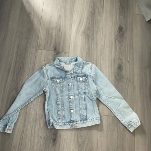 Ljusblå jeansjacka för barn  - Snygg ljusblå jeansjacka från Your Denim med klassisk krage, knappar framtill och två bröstfickor. Jackan är praktiskt taget ny skick om man bortser den lilla fläcken på baksidan av ärmen 