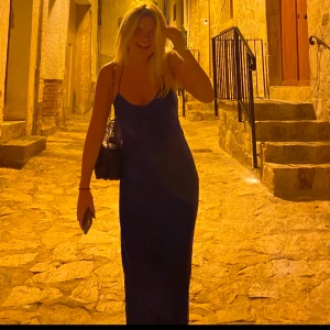 Blå långklänning med tunna axelband - Säljer en stilren långklänning i intensivt blått med tunna axelband och v-ringad hals. Klänningen har en slimmad passform och är tillverkad i ett glansigt, satinliknande material som ger en lyxig känsla. Perfekt för dig som vill sticka ut med en enkel men snygg look. Super fin klänning. Perfekt till sommaren 