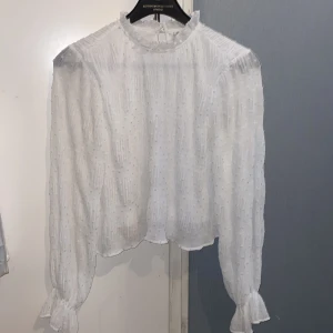 Vit blus med struktur från NLY Trend - Supersöt vit blus från NLY Trend i storlek 36. Blusen har hög krage med volang, transparent strukturtyg med diskreta prickar och långa ärmar med knyt vid handlederna. Perfekt för dig som gillar romantiska detaljer och en luftig känsla. Jag har aldrig använt den fick den av mamma som present för typ 3 månader sen! Den är perfekt för sommaren då den är väldigt luftig :) Jag kan självklart skicka bilder på det är bara att säga till 🫶🏻
