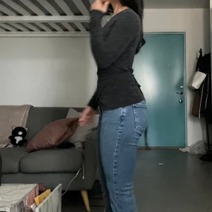 Mörkgrå omlottop med v-ringning - Säljer en mörkgrå långärmad omlottop med v-ringning. Tröjan har en tight passform och är tillverkad i ett mjukt, stickat material som sitter snyggt mot kroppen. Perfekt för dig som gillar en stilren och enkel look.