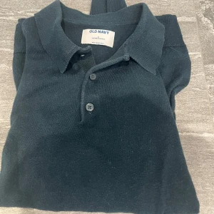 Mörkblå stickad pikétröja Old Navy - Snygg mörkblå stickad pikétröja från Old Navy med klassisk krage och två knappar framtill. Köpt i New York endast använd ett fåtal gånger! Tveka inte på att höra av dig vid minsta funderingar!