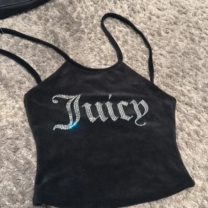 Juicy Couture svart sammetstopp - Supersnygg svart linnetopp från Juicy Couture i mjuk sammet med tunna axelband. Framsidan har glittrande strassbokstäver som stavar 'Juicy' och ger en lyxig vibe. 