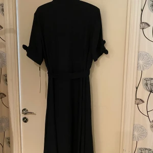 Helt ny Mörkblå lskjortklänning från Calvin Klein - Mörkblå lskjortklänning från Calvin Klein med klassisk skjortkrage, knytband i midjan och korta ärmar med knytdetalj. Stilren och tidlös design som ger en snygg siluett. Perfekt för dig som gillar minimalistisk och elegant look.