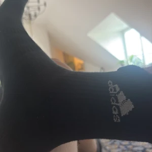 Svarta Adidas strumpor med logga - Svarta ribbade strumpor från Adidas med den klassiska vita loggan på sidan. Perfekta för dig som gillar sportig stil och vill ha bekväma strumpor med snygg design.