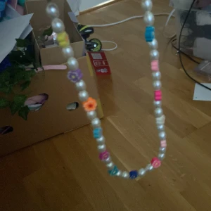 Pärlhalsband med färgglada blommor - Superfint halsband med vita pärlor och färgglada blommor i olika nyanser. Halsbandet har en lekfull och trendig stil med inslag av rosa, blått, lila, orange och gult. Perfekt accessoar för att liva upp din outfit!