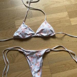 Vit bikini med rosa blommor - Säljer denna bikinin då den inte passar. Den är aldrig använd utan bara testad utanpå underkläder. Både under och överdelen är knyt.