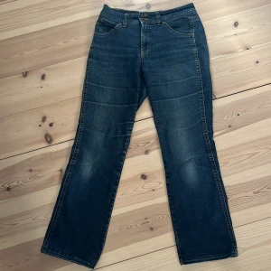 flared jeans - Snygga blå flared jeans och klassisk femficksdesign. Jeansen har dekorativa bakfickor med lock och knapp, samt tydliga kontrastsömmar. Tillverkade i slitstarkt denim med en mörk tvätt och subtila slitningar för en cool look. 
