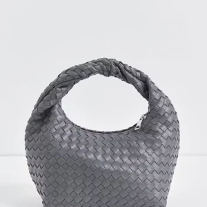 Grå flätad fina väska - Säljer en snygg slutsåld grå handväska med flätad design och rundad form. Väskan har ett kort handtag och stängs med dragkedja. Tillverkad i skinn och perfekt för dig som gillar stilrena accessoarer med en twist.
