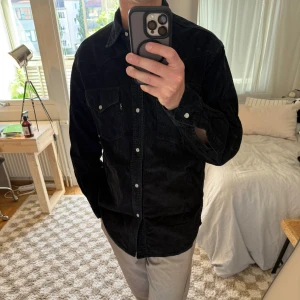Svart manchesterskjorta från Levi's S - Säljer en svart manchesterskjorta från Levi's i storlek S. Skjortan har klassisk westernstil med två bröstfickor och tryckknappar. Skjortan är lång i modellen.