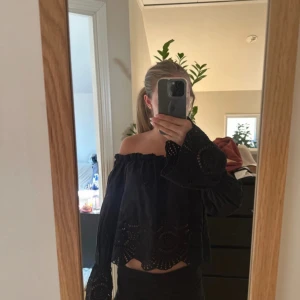 Svart offshoulder blus från Stradivarius - Svart offshoulder blus från Stradivarius med vida ärmar och broderade detaljer. Toppen är croppad och har ett snyggt hålmönster längs nederkanten och ärmsluten. Perfekt för dig som gillar en boho-inspirerad stil. I väldigt bra skick