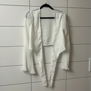 Vit topp som man knyter runt midjan  - Perfekt för att lyfta vilken outfit som helst med sin stilrena look.