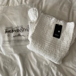 Vit kort klänning från TwoWinStyle - Supersöt vit kort klänning från TwoWinStyle med smockad överdel och volangig kjol 🤍. Klänningen har broderade detaljer och tunna axelband. Perfekt för sommarens alla tillfällen och ger en fräsch och trendig look. Den är ALDRIG använd! 