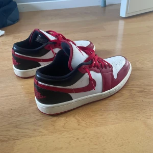 Nike Air Jordan 1 Low röd/vit - Snygga Nike Air Jordan 1 Low sneakers i klassisk röd, vit och svart färg. Skorna har röd snörning, perforerad tå och ikoniska Jordan-loggor på häl och plös. Ovandelen är i skinn och textil, med låg profil och platt sula för en clean streetstil. Använda fåtal gånger. Du får med ett par creaseskydd och cleaning wipes!